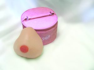 A prosthetic breast is leaning upright against a pink case designed for holding the prosthetic.